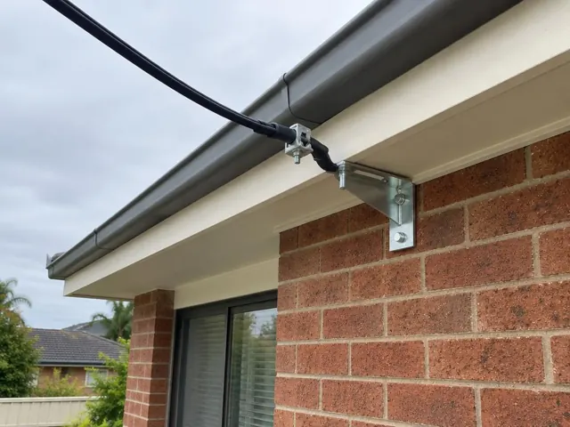 Overhead service cable and point-of-attachment bracket on a brick house eave in Melrose Park